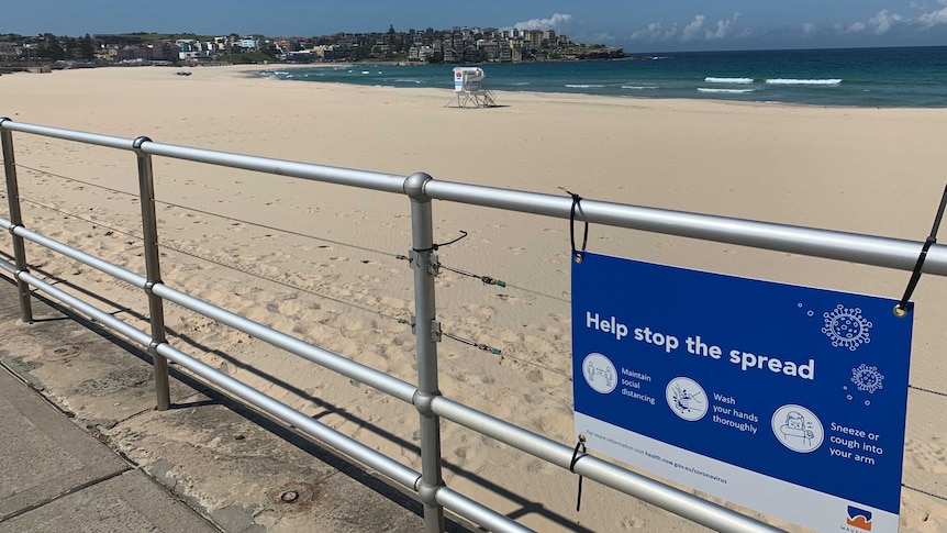 The empty sand of bondi beach and a sign advising coronavirus directives
