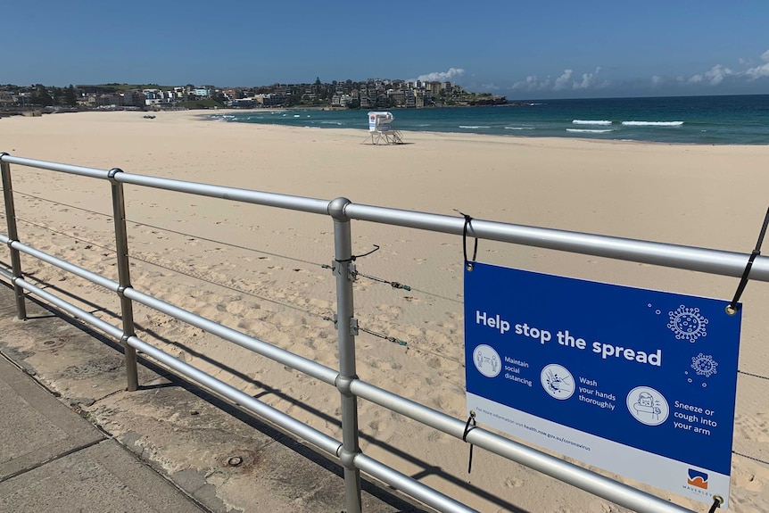 The empty sand of bondi beach and a sign advising coronavirus directives