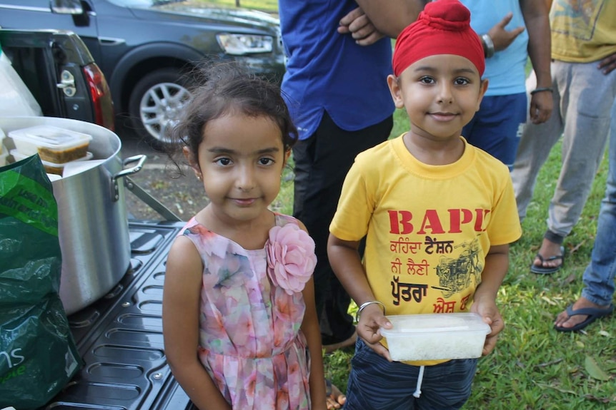 A small girl and boy hold a food container.