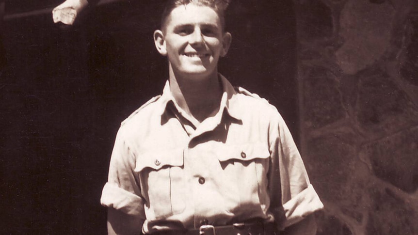 A young man in army uniform standing outside a stone building.