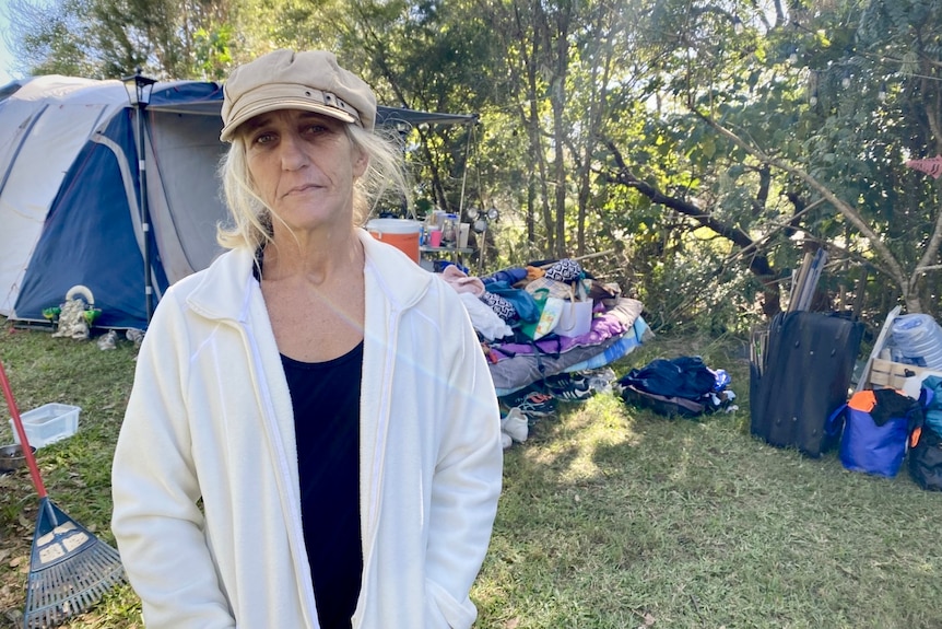 a woman in cap and jacket stands in front of her tentsite 