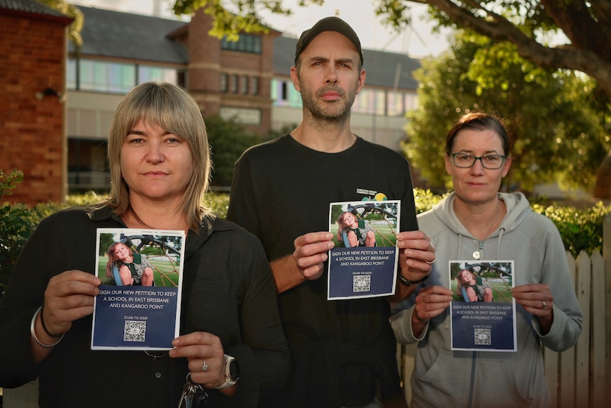 Three parents hold flyers with a QR code to sign the petition to save East Brisbane State School