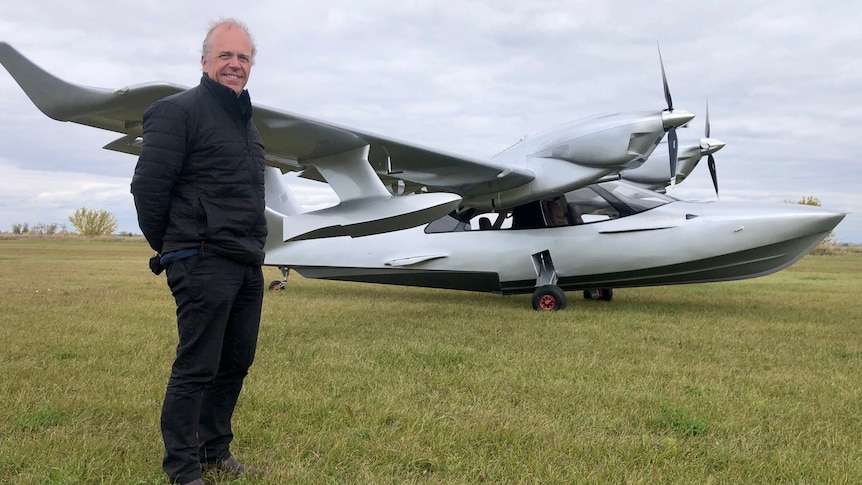 Michael Smith stands in an open field in front of a silver amphibious seaplane