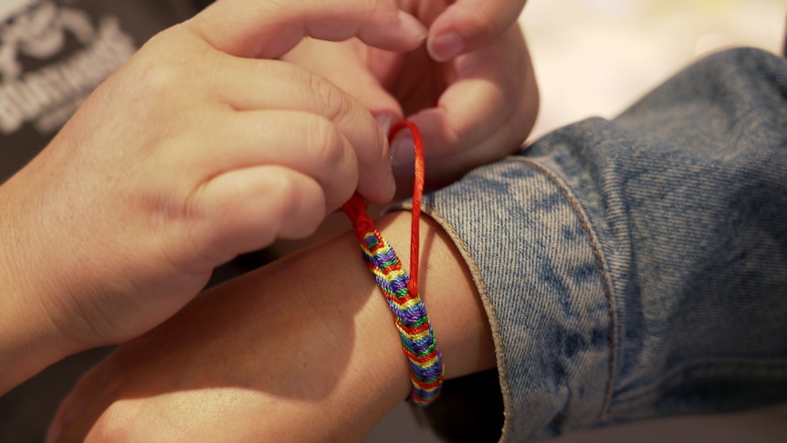 A woman's hands tying a bracelet to another woman's wrist