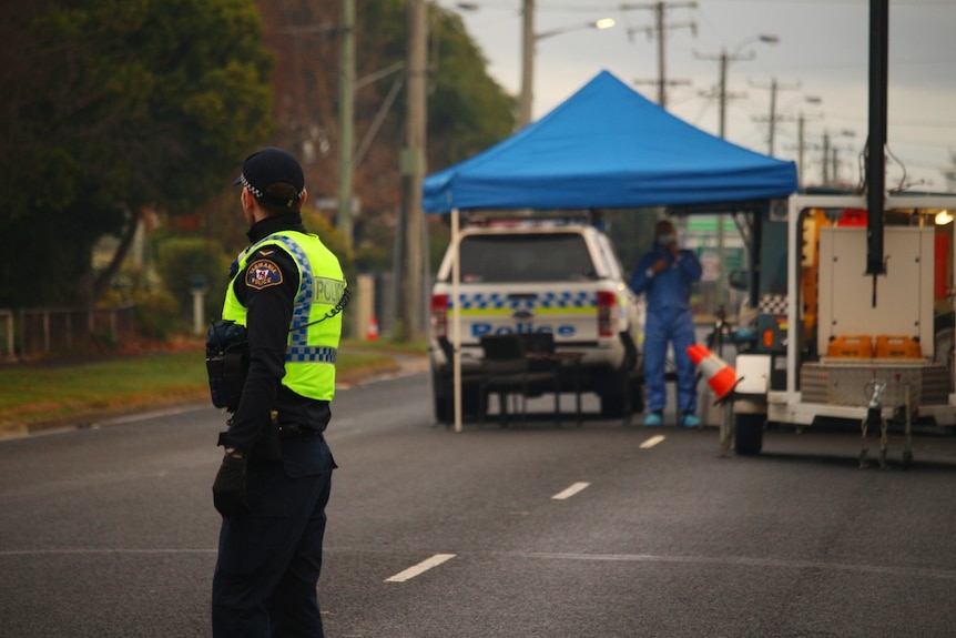 A Tasmania Police officer stands in foreground, with forensic investigator in background.