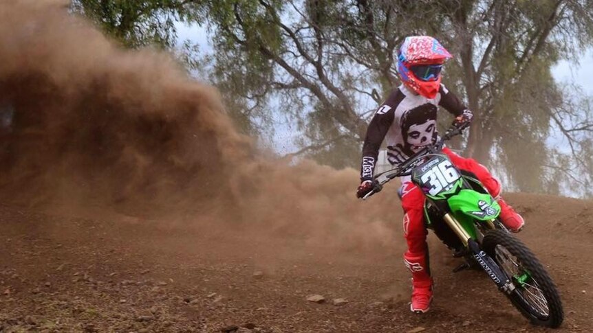 Ned Desbrow wearing a red helmet on a red dirt bike, doing a skid with red dust in the air.