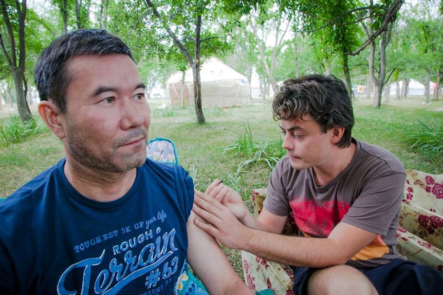 One man applies kambo to another man's arm in an outdoors ceremony.