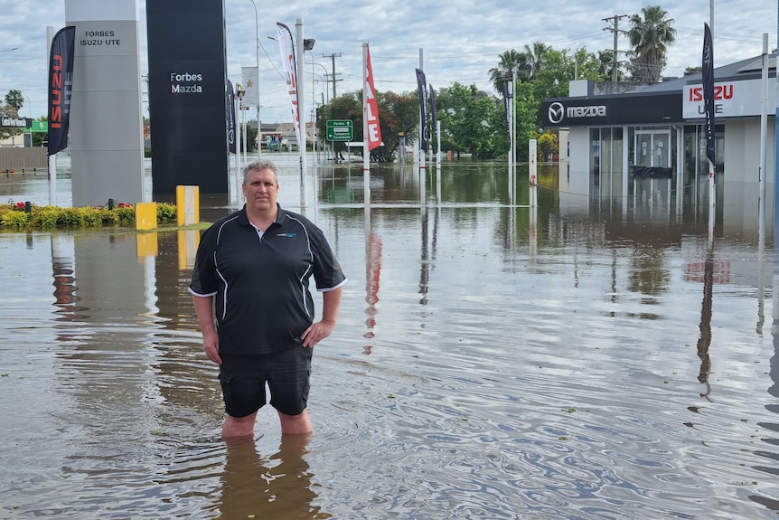 A man stands in floodwater up to his knees, in a street in a country town.