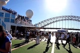 People stand around on a cruise ship with the Sydney Harbour Bridge in the background.