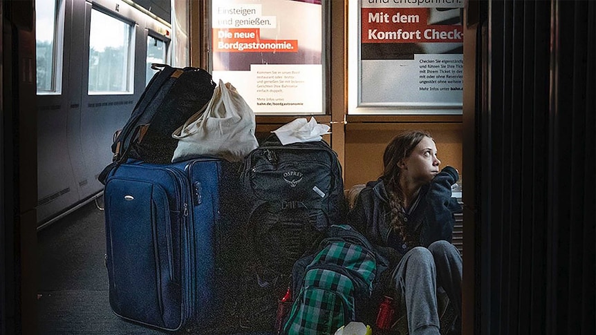 Climate activist Greta Thunberg sits on the floor of a train surrounded by luggage, gazing out a window.