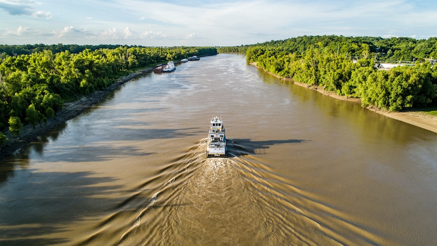 Overhead of boat travelling down a muddy-coloured river creating a wake. 