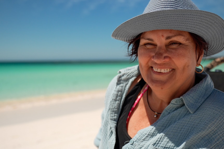 Woman wearing hat at the beach smiling in front of turquoise water