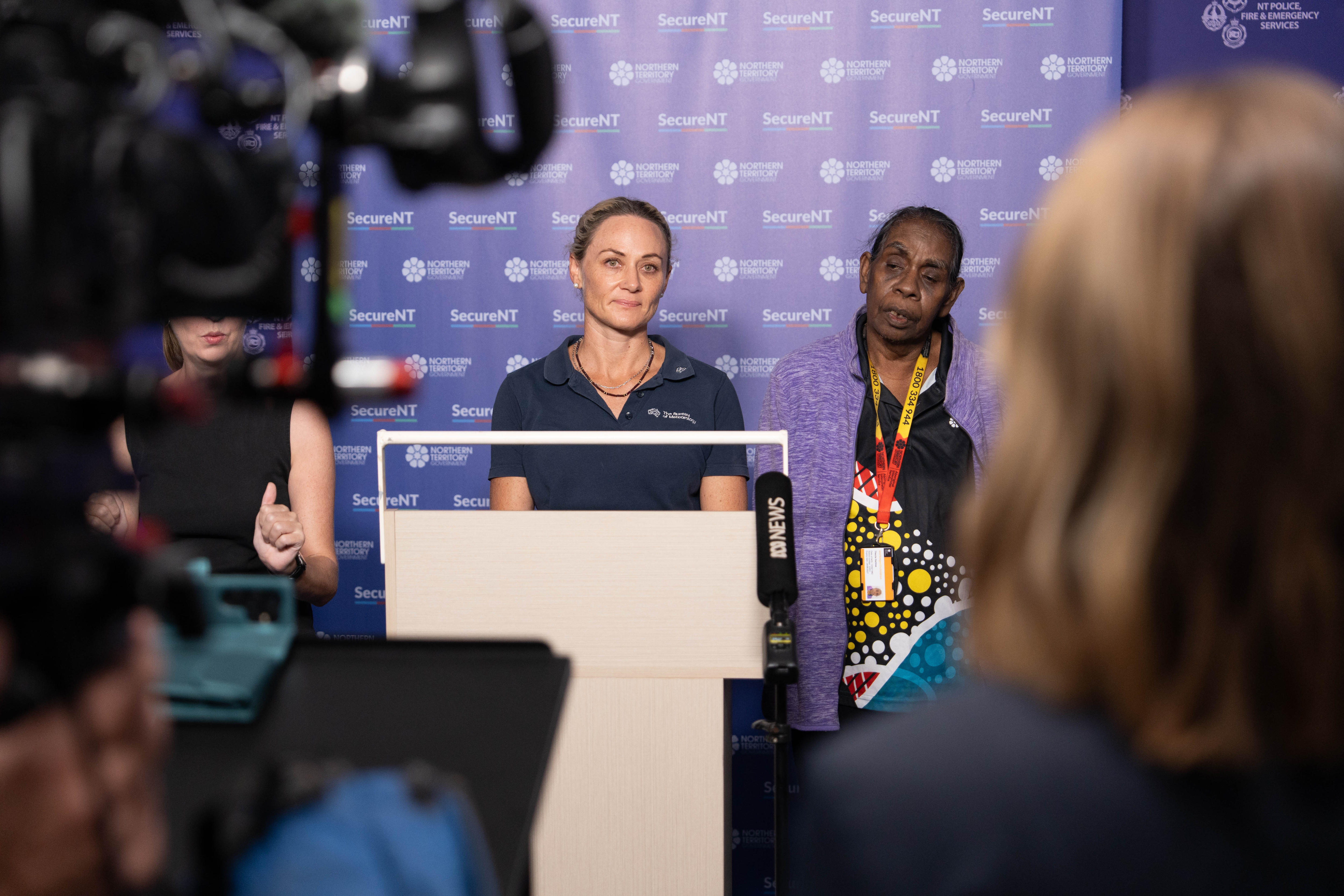 Una mujer parada frente a un atril habla con un grupo de prensa en una sala.