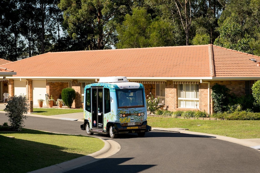 A small vehicle travels along a road in a retirement village.