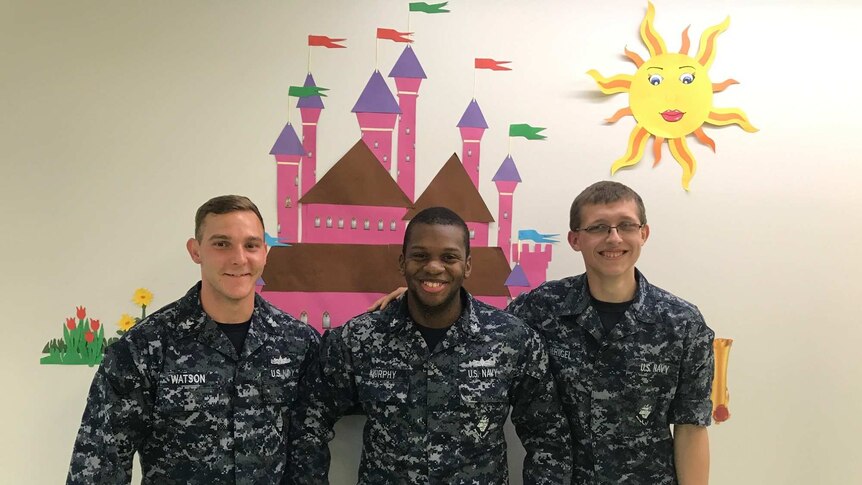Three US Sailors Stand In Front of A Princess Castle at a Children's Hospital