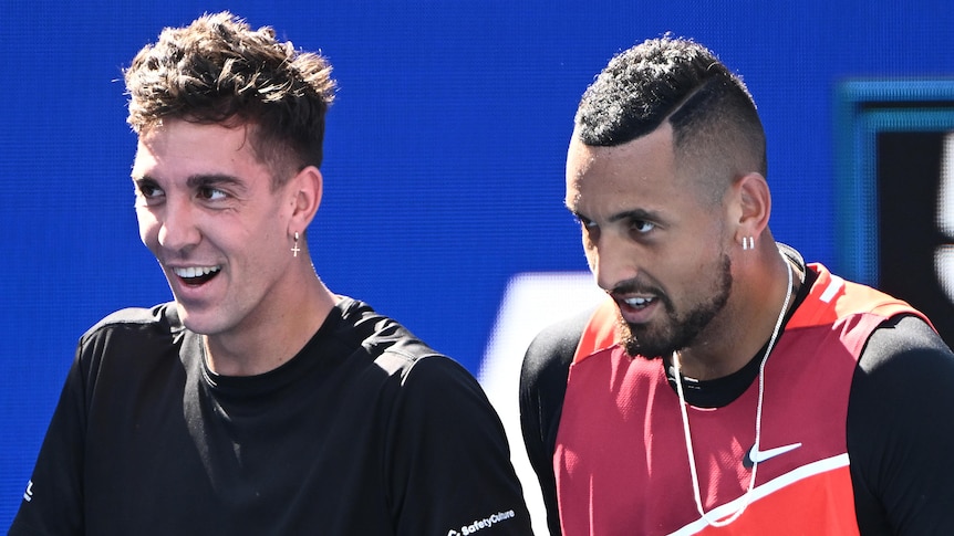 Two Australian male tennis players smle and laugh during a doubles match.