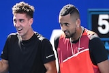 Two Australian male tennis players smle and laugh during a doubles match.