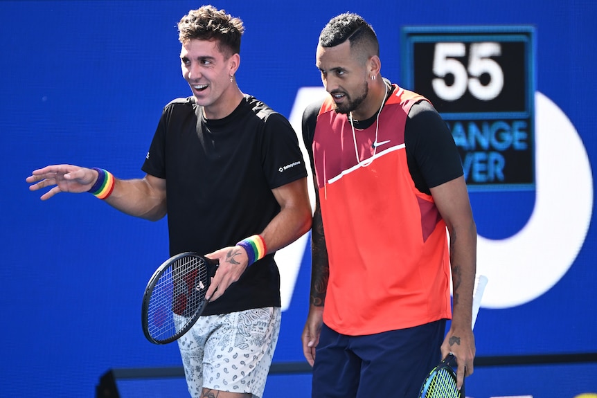 Two Australian male tennis players smle and laugh during a doubles match.