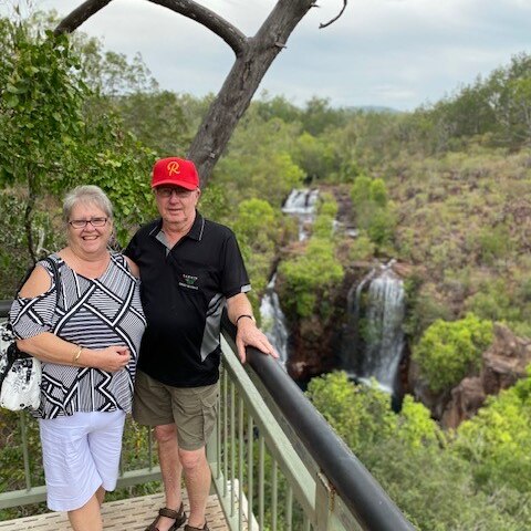A woman in a black and white top and a man in a black top and red hat stand next to rail over looking a waterfall. 