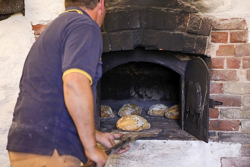 A man pulls loaves of bread out of an old-fashioned, underground oven.