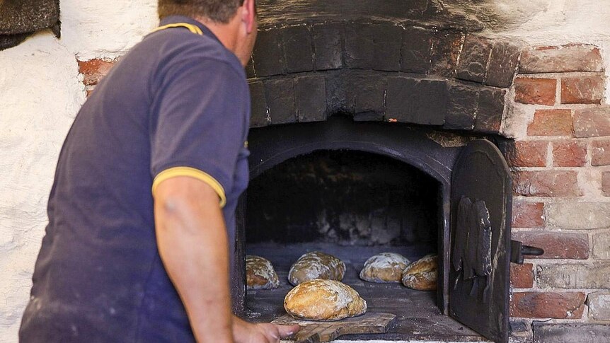 A man pulls loaves of bread out of an old-fashioned, underground oven.