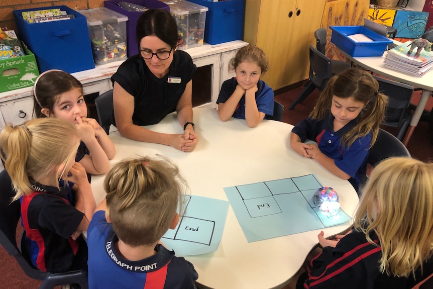 A teacher sits around a small table with a group of young students.