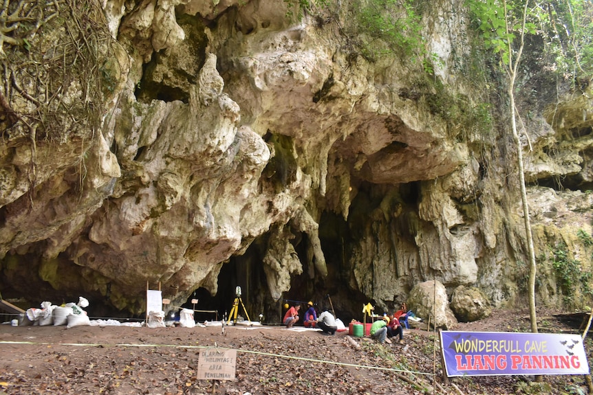 People crouched in front of a big cave entrance