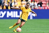 A woman soccer player wearing yellow and green dribbles during a game