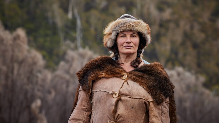 Gina Chick standing in the wilderness in an animal-skin coat and hat.