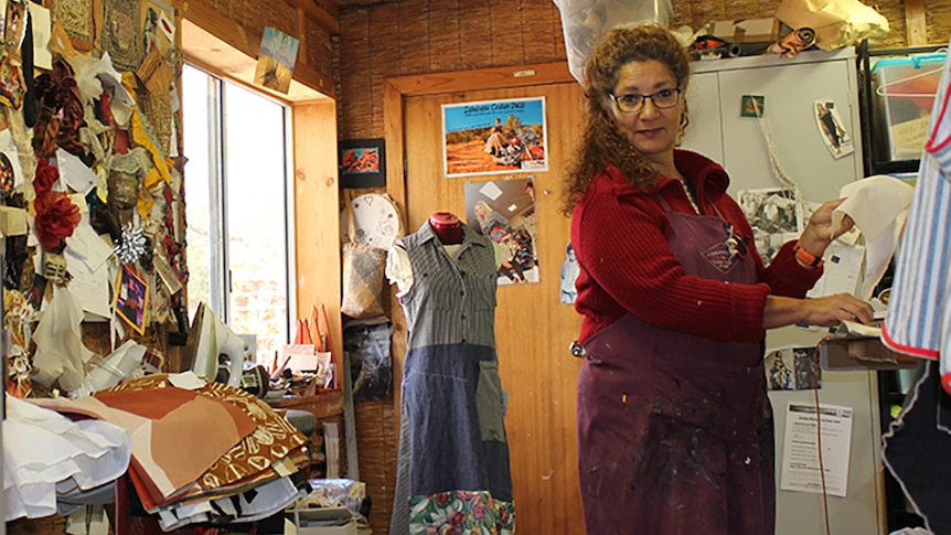 A woman with curly red hair stands in a sewing room.