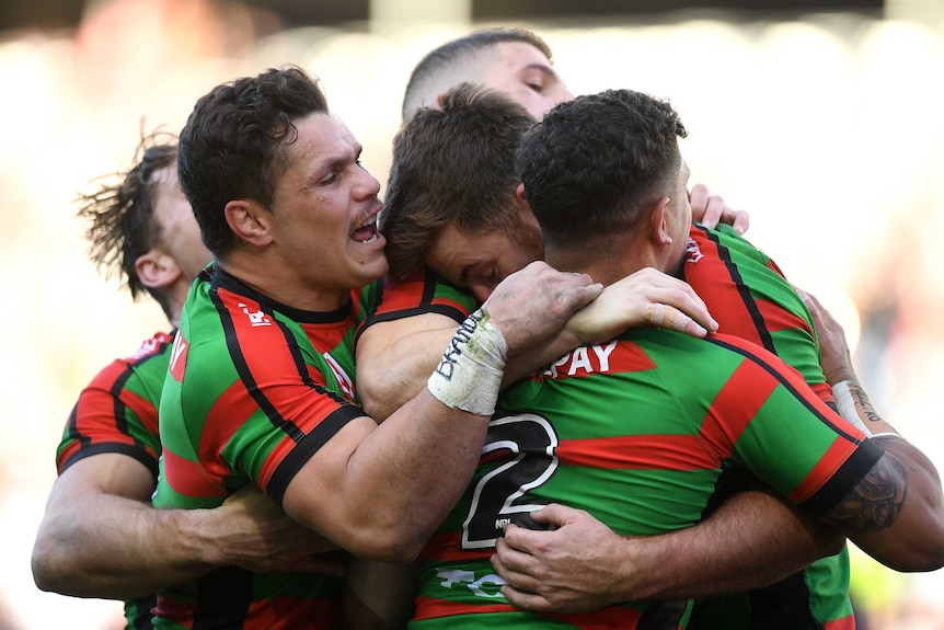 Five male NRL players embrace as they celebrate a try scored by their team.