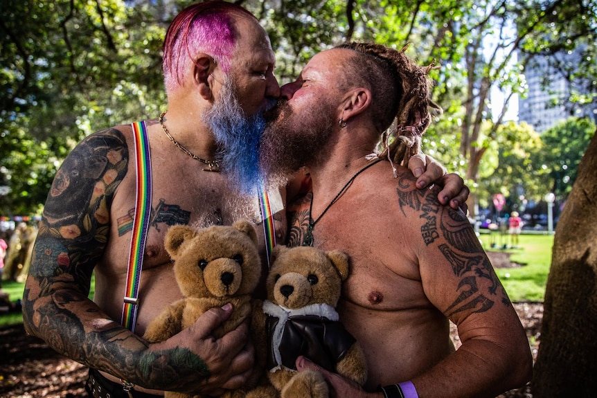 Two men hugging and kissing a teddy bear