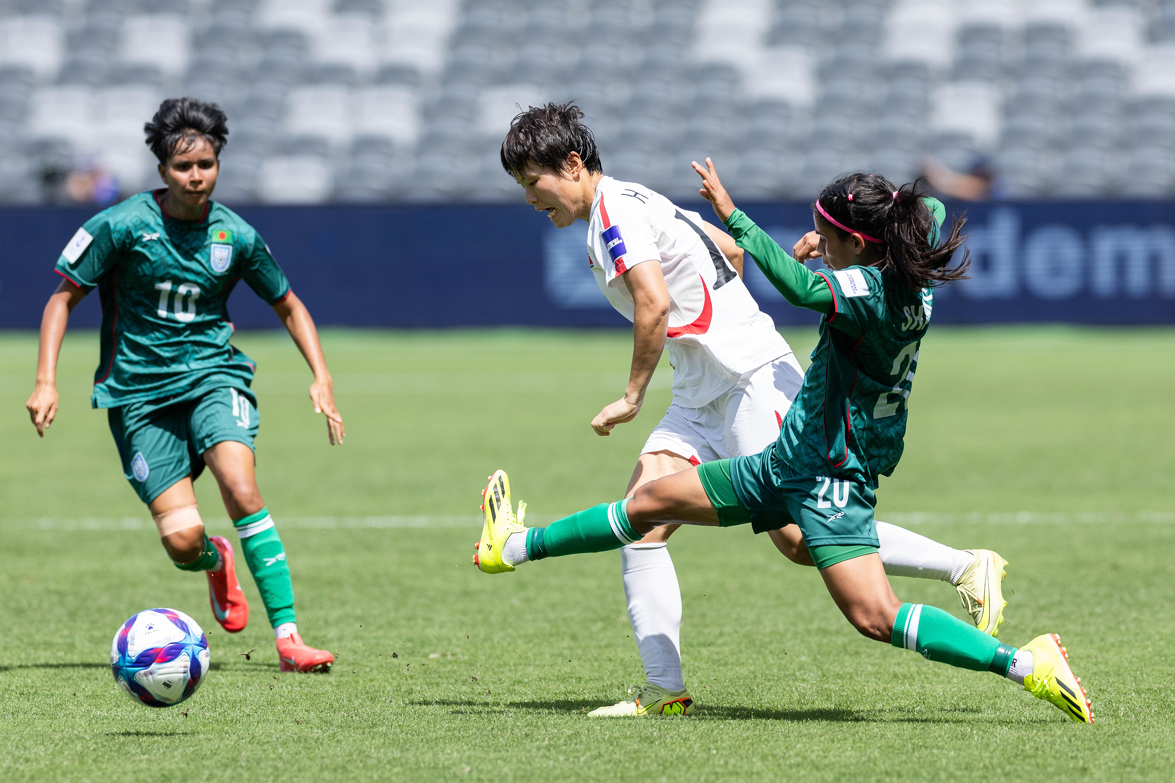 Soccer players in white and in blue tussle for the ball in bright sunshine
