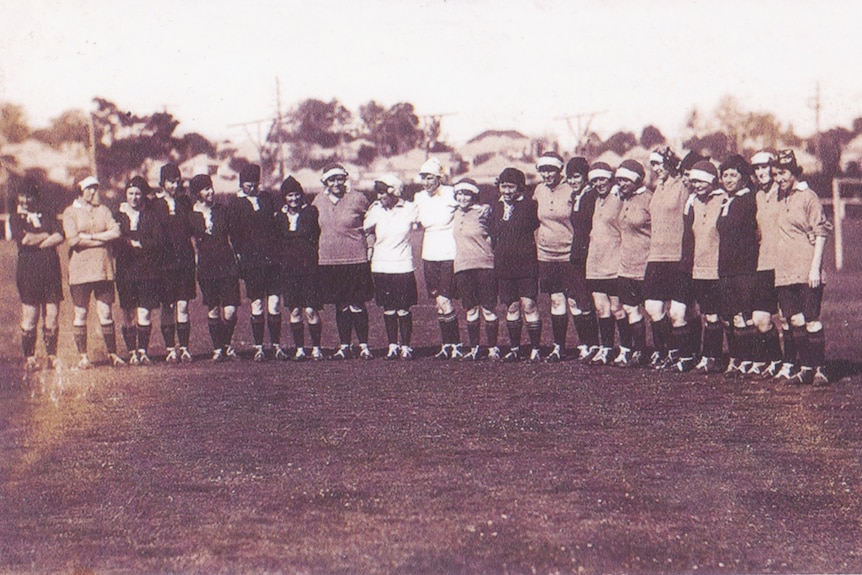 A black and white image of ladies lined up in front of a soccer goal.