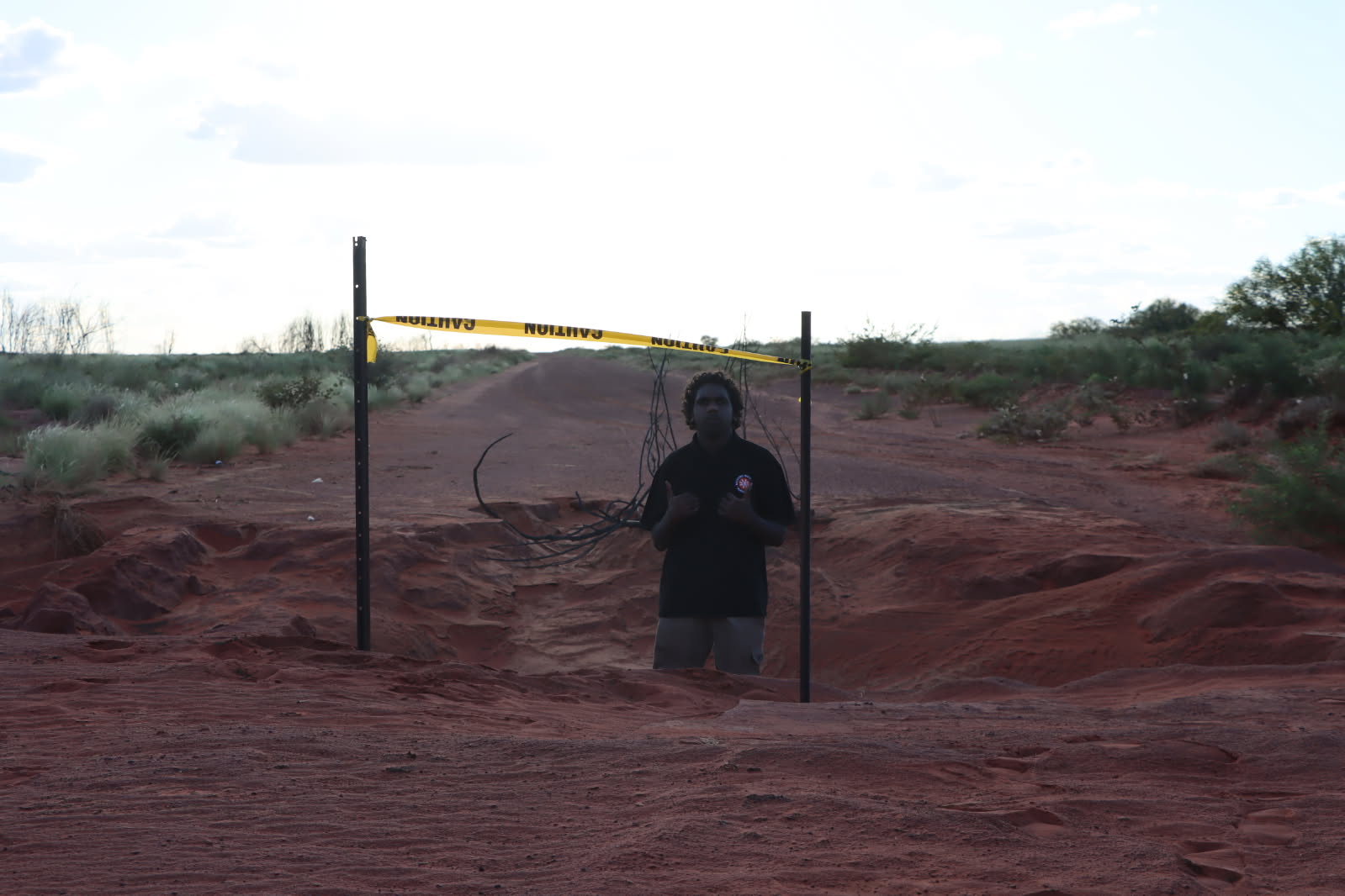 A man gives a double thumbs up from a hole in the middle of the road.
