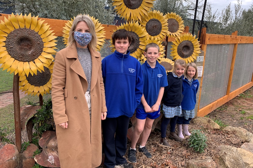 A woman standing with four children with metal sunflowers in the background