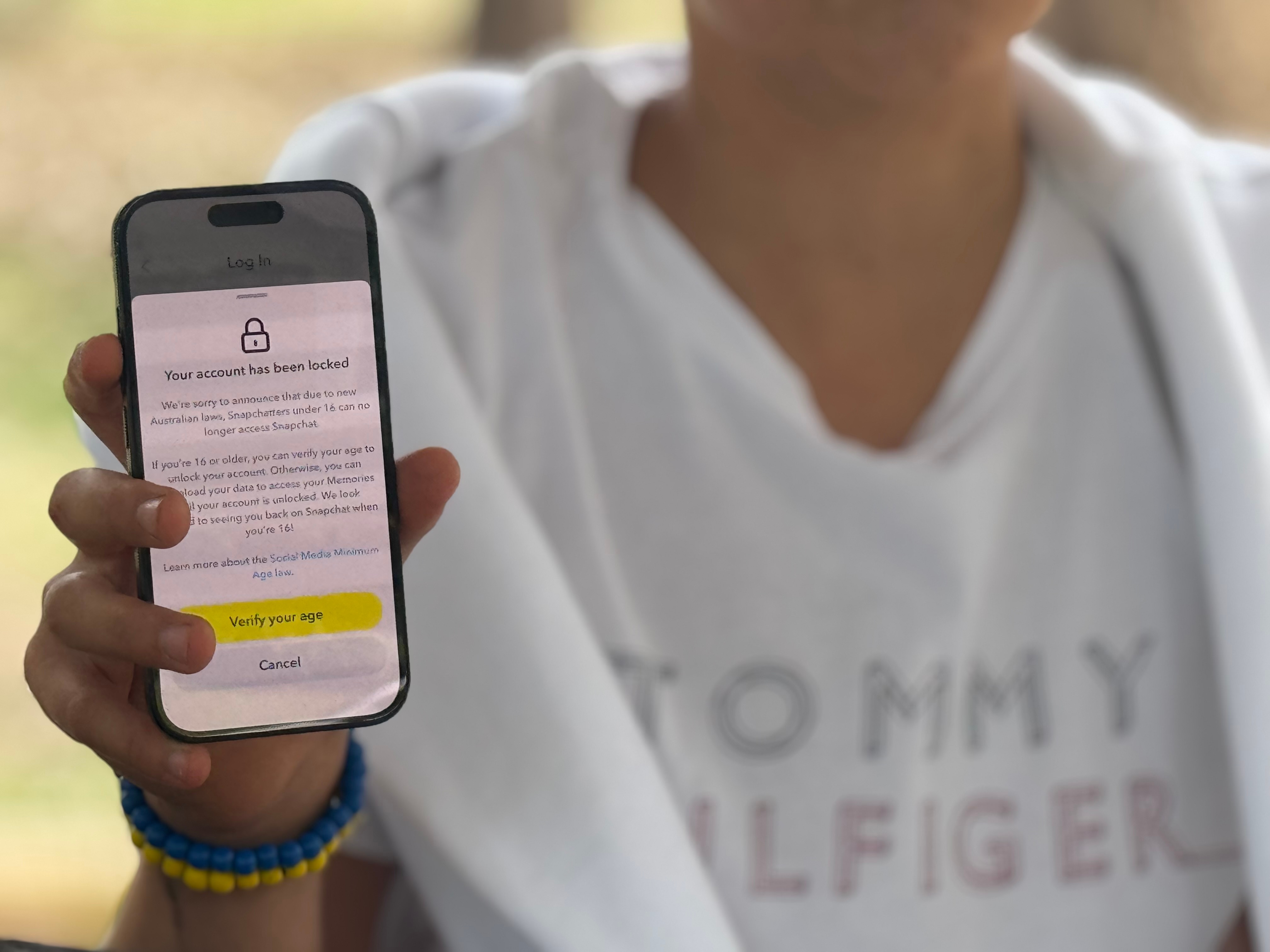 Um menino de camisa branca segurando um telefone celular.