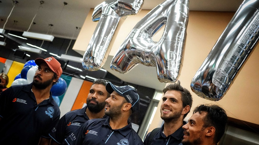 Members of the Buffaloes with their arms around each others' shoulders, underneath silver balloons spelling TAI.