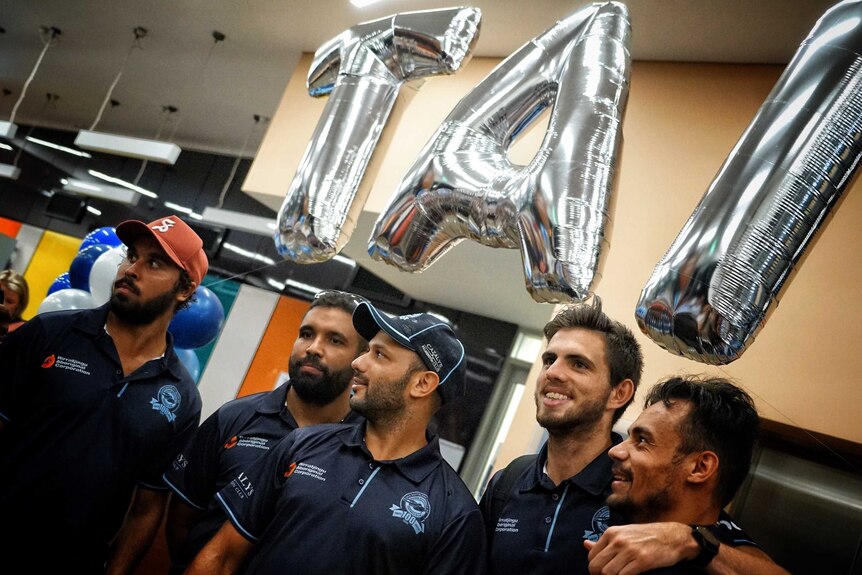 Members of the Buffaloes with their arms around each others' shoulders, underneath silver balloons spelling TAI.
