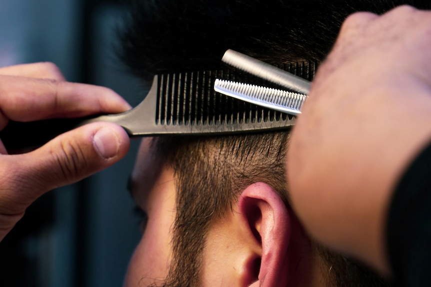 A close up of a man having his hair cut by a barber with scissors.