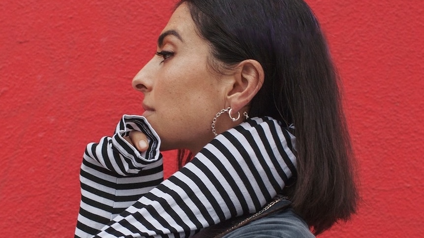 anna lunoe standing side on in front of a red wall