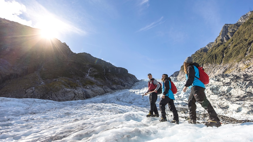 Three people walking along a glacier during the day.