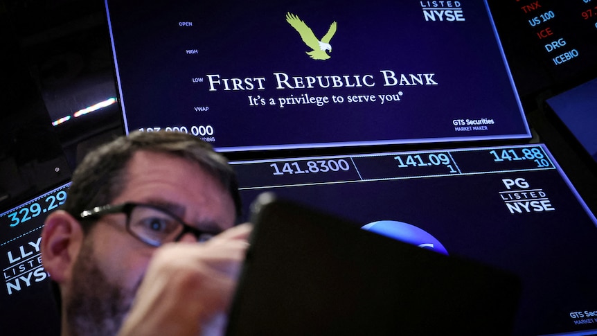 a trader wearing glasses works at the post where First Republic stock is traded at the NYSE