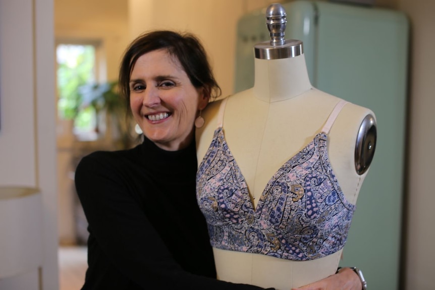 A woman wearing black hugs a mannequin with a blue pattern bra on it.