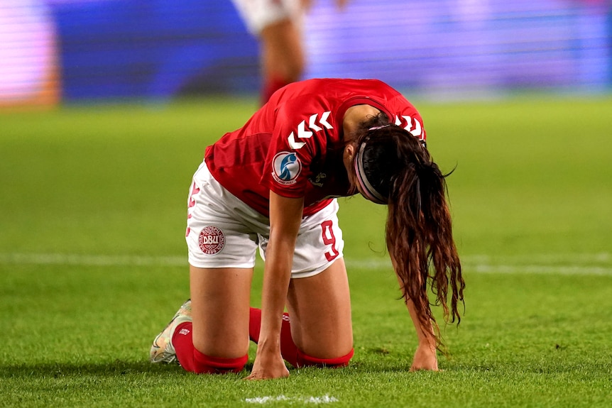 A soccer player wearing red and white uniform leans on her hands and knees during a game
