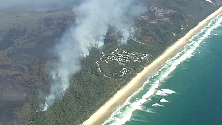 The township of Teewah with plumes of smoke rising around it and large stretches of burnt bush behind it.