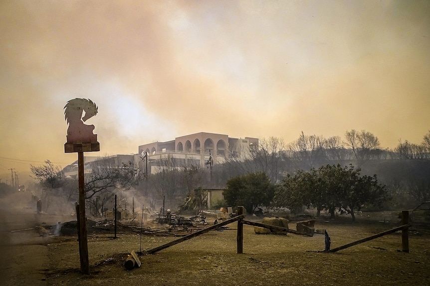 Yunanistan'ın Rodos kentinde bir tepenin üzerindeki bir yapının üzerindeki orman yangınından çıkan dumandan gökyüzü sarıya dönüyor