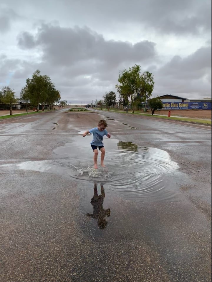 Little boy jumps in rain puddle in the middle of the street