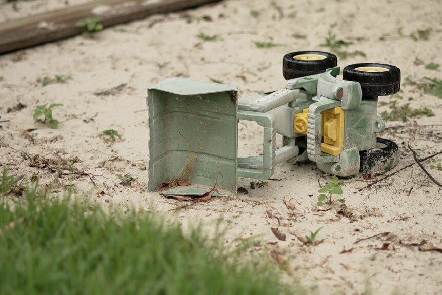 A toy digger lays on its side in a sandpit.