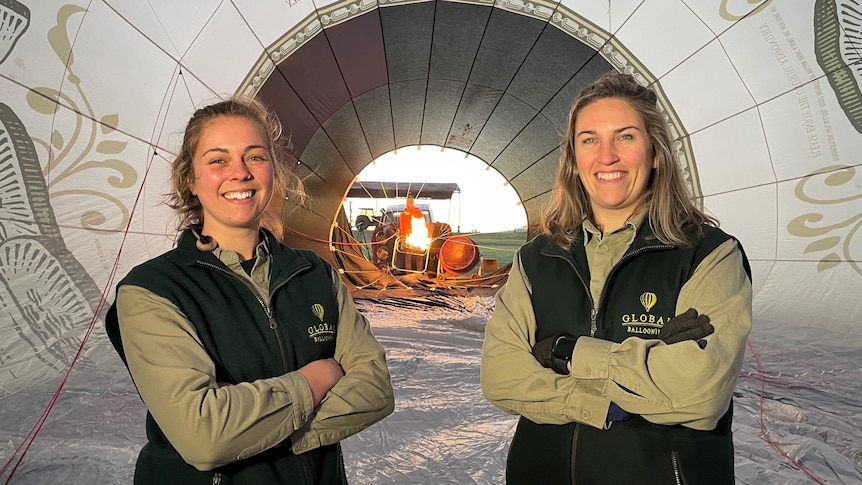 Two girls stand inside a hot air balloon with their arms crossed